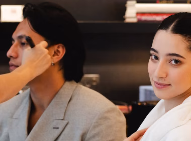 Ameera Khan tersenyum ke arah kamera sambil Jefri Nichol sedang disolek di belakang.