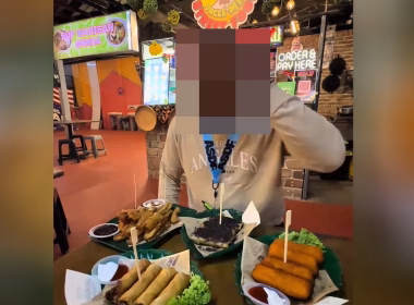 Pengulas makanan sedang duduk di hadapan beberapa hidangan risol di sebuah gerai makanan jalanan bertemakan hipster
