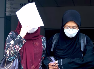 Dua wanita memakai pelitup muka, salah seorang menutup muka dengan kertas semasa keluar dari bangunan mahkamah.