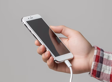 Tangan memegang iPhone yang sedang dicas dengan kabel