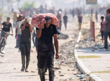 Orang awam Palestin membawa barang keperluan sambil berjalan di jalan berdebu yang rosak.