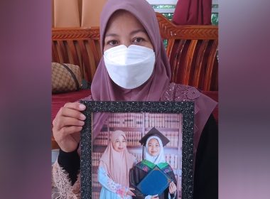 Seorang wanita berhijab dan memakai pelitup muka memegang bingkai gambar anaknya dalam pakaian konvokesyen.