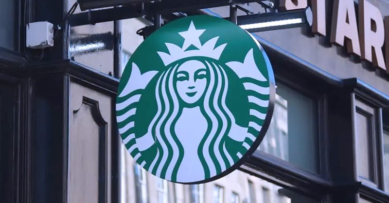 Papan tanda bulat Starbucks berwarna hijau dan putih tergantung di hadapan sebuah kedai.