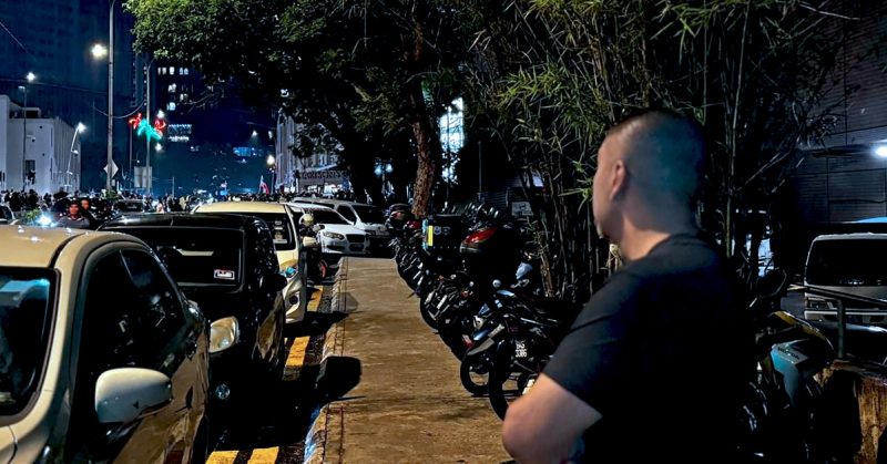 ADUN Duyong berdiri di tepi laluan pejalan kaki waktu malam sambil memerhati suasana jalan yang sesak dengan kenderaan dan motosikal, berhadapan kawasan tumpuan awam.