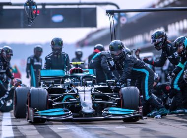 Sebuah kereta Formula 1 sedang berhenti di pit lane dengan kru pasukan giat melakukan kerja menukar tayar dan servis pantas.