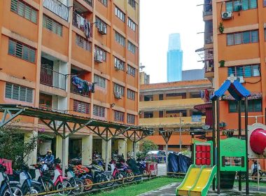 Sebuah flat kos rendah berwarna jingga dengan kawasan permainan kanak-kanak dan motosikal parkir di hadapan.