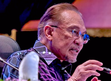 Perdana Menteri Malaysia sedang bercakap di hadapan mikrofon semasa sesi rasmi.
