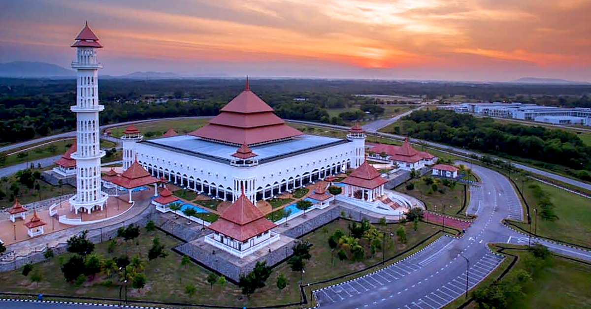 Pemandangan udara Masjid Taman Ilmu di Tembila, Besut, Terengganu dengan menara tinggi dan bumbung merah berlatar matahari terbenam.