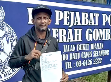 Mamak Puteh memegang laporan polis di hadapan papan tanda Ibu Pejabat Polis Daerah Gombak.