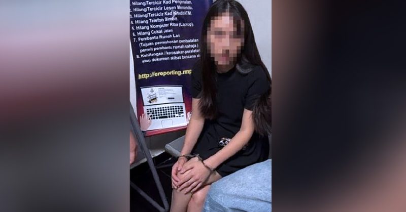 Wanita berambut panjang berpakaian serba hitam, duduk sambil tangan bergari di hadapan poster panduan laporan polis.