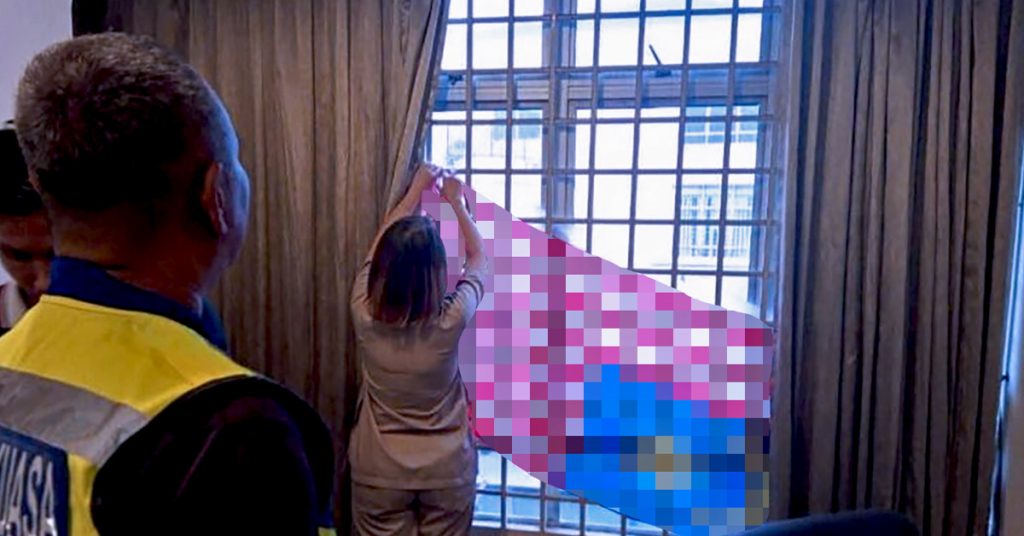 Seorang wanita menurunkan Jalur Gemilang di tingkap sambil diperhatikan pegawai penguat kuasa.