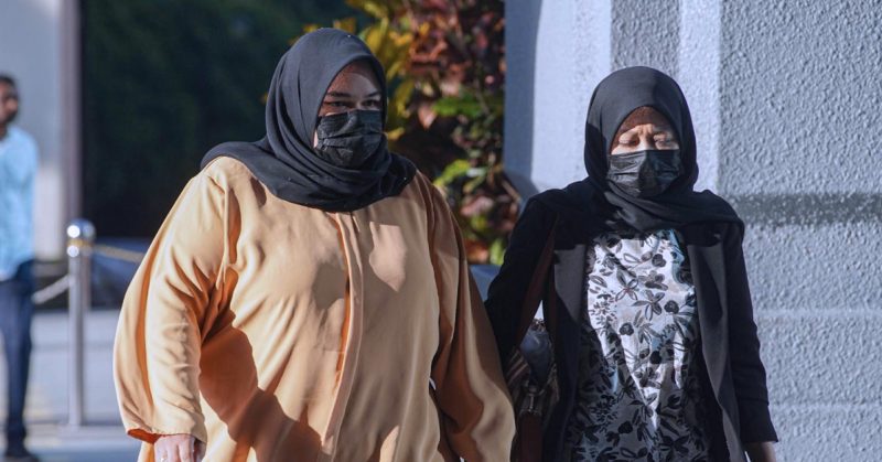 Dua wanita berhijab dan bermasker berjalan beriringan menuju bangunan mahkamah.