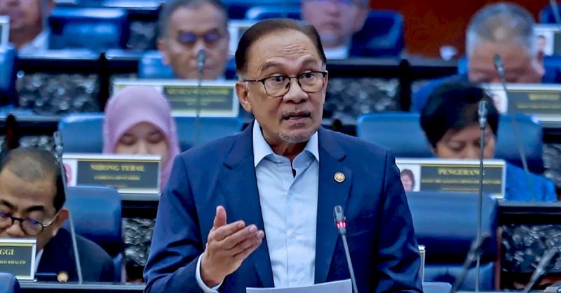 Perdana Menteri Malaysia berucap di Dewan Rakyat sambil memegang kertas dan mengangkat tangan.