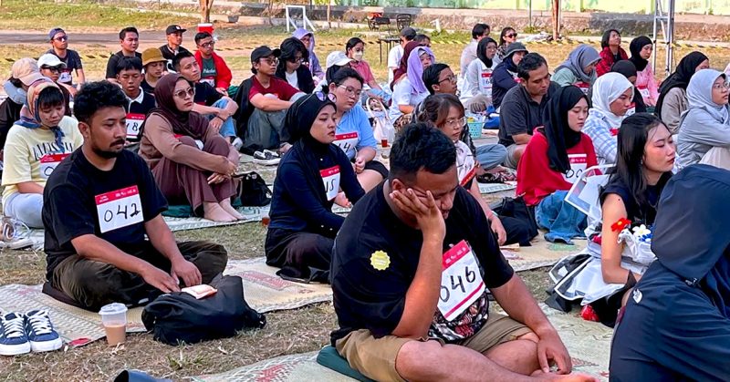 Sekumpulan peserta duduk di atas tikar sambil termenung, memakai nombor peserta, dalam pertandingan mengelamun di Yogyakarta.