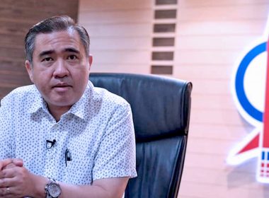 Anthony Loke duduk di meja pejabat dengan logo roket DAP di belakangnya.