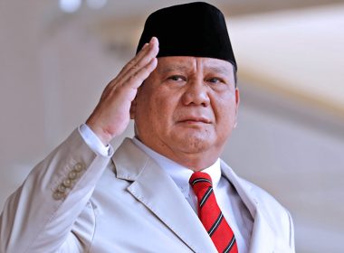 Presiden Indonesia Prabowo Subianto memberi tabik hormat dengan berpakaian sut rasmi dan songkok hitam.