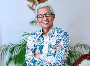 Duta Besar Indonesia ke Malaysia tersenyum sambil berpeluk tubuh, berlatarbelakangkan bendera Indonesia dan Malaysia.