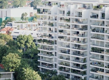 Pemandangan sebuah kondominium moden bertingkat tinggi dengan balkoni penuh tanaman hijau, menggambarkan gaya hidup urban yang sering diiklankan.