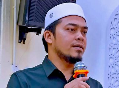 Ketua Pemuda PAS Perak memegang mikrofon ketika berucap di sebuah majlis, berlatar dinding bercorak Islamik.