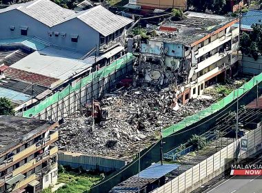 Imej udara menunjukkan kerja perobohan blok flat lama di Kampung Sungai Baru, dengan jentera berat meruntuhkan bangunan dan timbunan konkrit memenuhi kawasan.