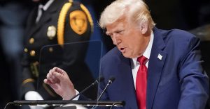 Donald Trump berucap dengan penuh semangat di pentas PBB, memakai sut biru gelap dan tali leher merah.