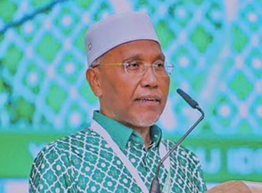 Idris Ahmad berucap di pentas PAS dengan latar hijau bermotif Islamik, berpakaian baju corak hijau putih dan songkok putih.