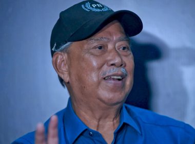 Tan Sri Muhyiddin Yassin memakai topi PN dan berbaju biru, tersenyum ketika bercakap dalam satu program politik.