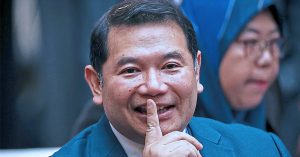 Rafizi Ramli tersenyum sambil meletakkan jari di bibir ketika menghadiri majlis rasmi.