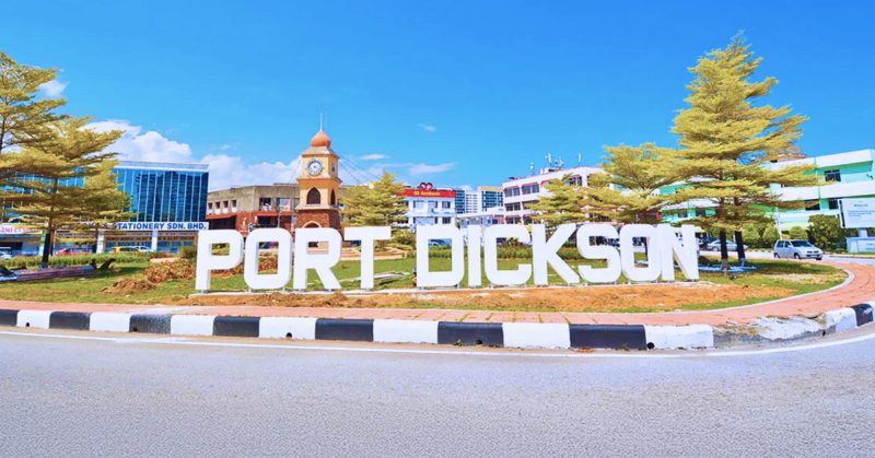 Tugu tulisan besar "Port Dickson" di bulatan bandar, dengan latar bangunan dan menara jam, ikon pelancongan Negeri Sembilan.