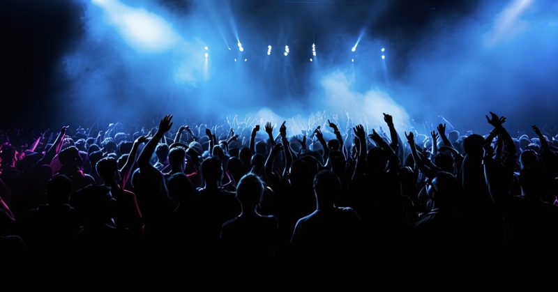 Penonton konsert Malaysia bersorak dalam suasana meriah dengan cahaya biru ungu, berkaitan garis panduan PUSPAL tentang pakaian.