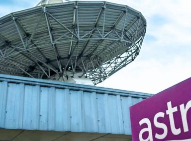 Logo Astro di hadapan bangunan dengan antena satelit besar di latar belakang, melambangkan syarikat penyiaran dan televisyen berbayar Malaysia.
