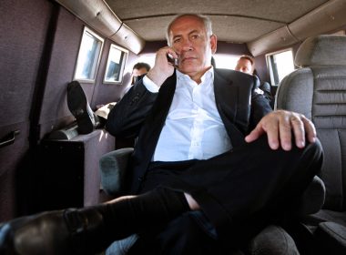 Benjamin Netanyahu duduk dalam kenderaan sambil menggunakan telefon bimbit.