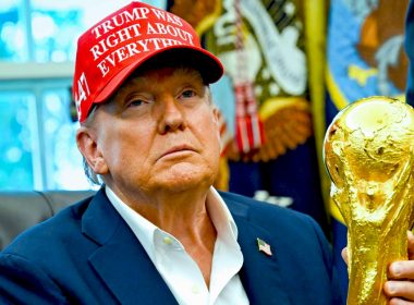 Donald Trump memakai topi merah dengan tulisan putih sambil memegang trofi Piala Dunia emas.