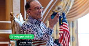 Perdana Menteri Anwar Ibrahim tersenyum sambil berbual telefon dengan Donald Trump, Presiden Amerika Syarikat, sambil berlatarbelakangkan bendera Malaysia dan AS.