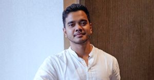 Alif Satar memakai kemeja putih berdiri santai di dalam bangunan dengan latar dinding lembut dan pencahayaan semula jadi.