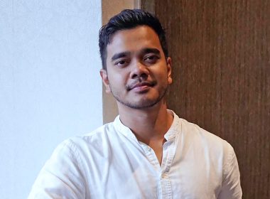 Alif Satar memakai kemeja putih berdiri santai di dalam bangunan dengan latar dinding lembut dan pencahayaan semula jadi.