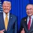 Donald Trump dan Anwar Ibrahim berpakaian sut formal berdiri bersebelahan di hadapan latar biru dengan bendera di belakang.