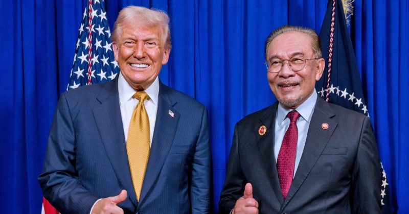 Donald Trump dan Anwar Ibrahim berpakaian sut formal berdiri bersebelahan di hadapan latar biru dengan bendera di belakang.