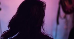 Seorang wanita berdiri membelakangi kamera dalam pencahayaan ungu dan merah jambu, menggambarkan suasana misteri dan identiti yang disembunyikan, berkaitan isu bakal pengantin tular.