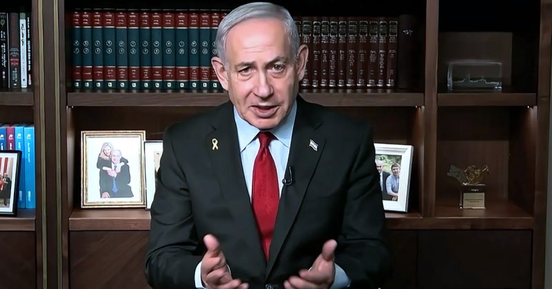 Benjamin Netanyahu duduk di hadapan rak buku sambil bercakap dalam temubual rasmi, mengenakan sut gelap dengan tali leher merah.