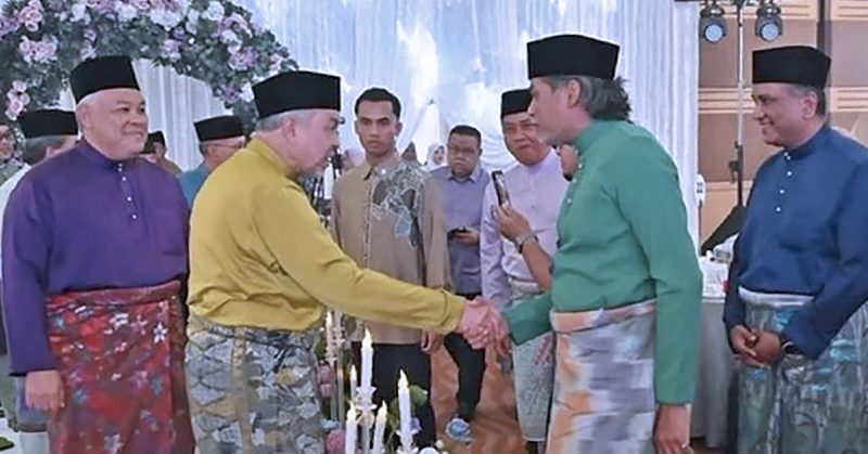 Sekumpulan lelaki berbaju Melayu sedang berjabat tangan di sebuah majlis rasmi; suasana sopan dengan dekorasi perkahwinan — KJ kembali ke UMNO.