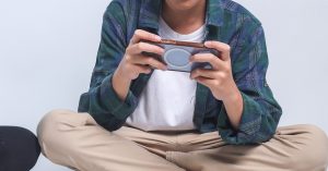 Seorang kanak-kanak duduk bersila sambil bermain telefon pintar; fokus pada penggunaan online game.