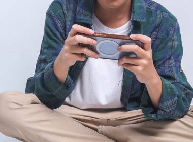 Seorang kanak-kanak duduk bersila sambil bermain telefon pintar; fokus pada penggunaan online game.