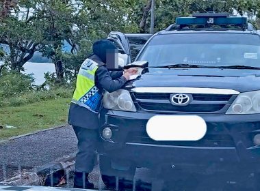 Pegawai JPJ wanita sedang menulis saman pada sebuah kenderaan Toyota hitam di tepi jalan, berkaitan kes pemandu e-hailing disaman kerana baju tidak berkolar.